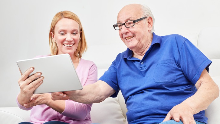 Young woman explains the social network and the video chat to a pensioner on the laptop