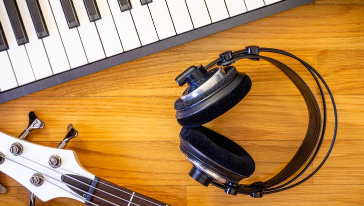 A wooden background with a set of musical instruments consisting of a keyboard, a bass guitar and a pair of headphones.