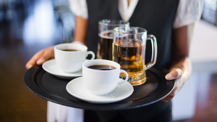 Mid section of waitress holding serving tray with coffee cup and pint of beer in restaurant