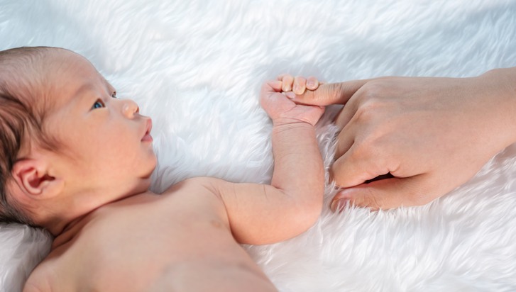 Spädbarn håller förälders finger