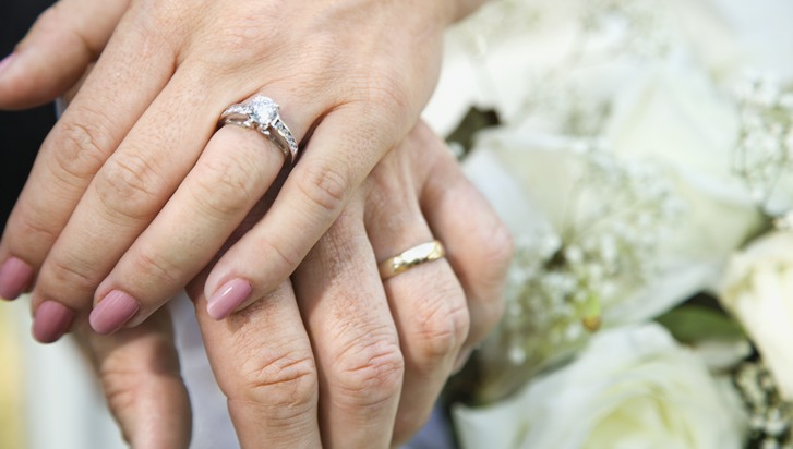 Close-up of bride and grooms hands overlapping.